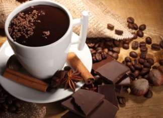 cup of hot chocolate, cinnamon sticks, nuts and chocolate on wooden table