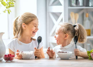 due bambine sorridenti mangiano cereali per la colazione